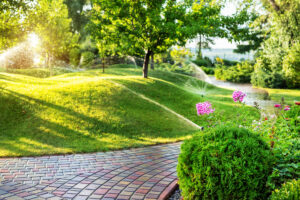 Bild zeigt eine professionelle Bewässerung einer hügeligen Gartenparkanlage. Im Vordergrund Busch und Blumen.